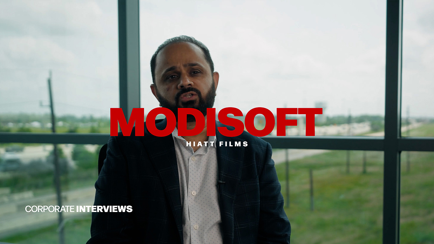 Corporate interview subject seated indoors with city view behind him filmed by Hiatt Films