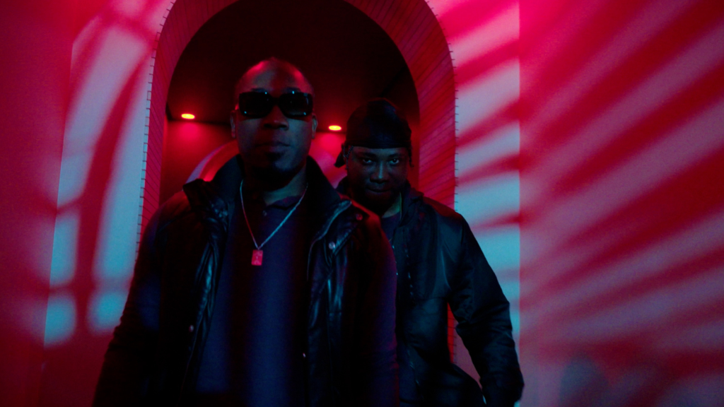 Two men walking through red-lit hallway in cinematic narrative scene