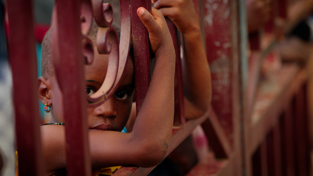 Young child looking through red metal gate during documentary filming