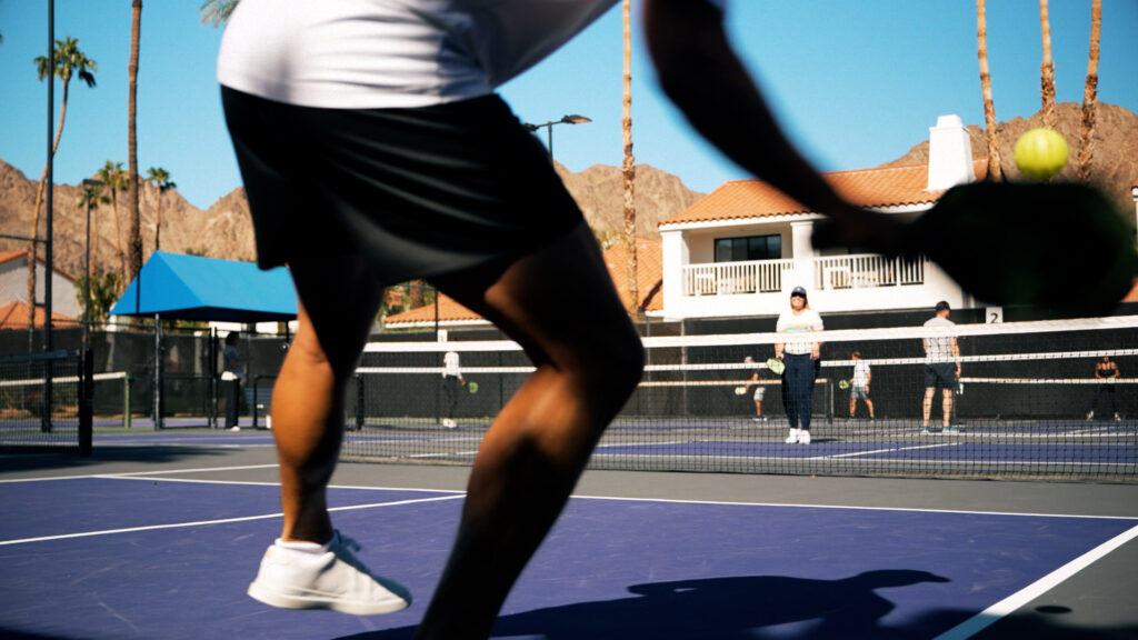 Pickleball players mid-action on outdoor court with ball in motion