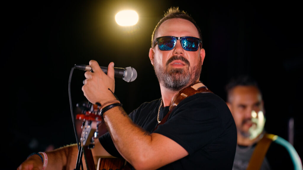Male singer performing live with microphone and sunglasses on stage
