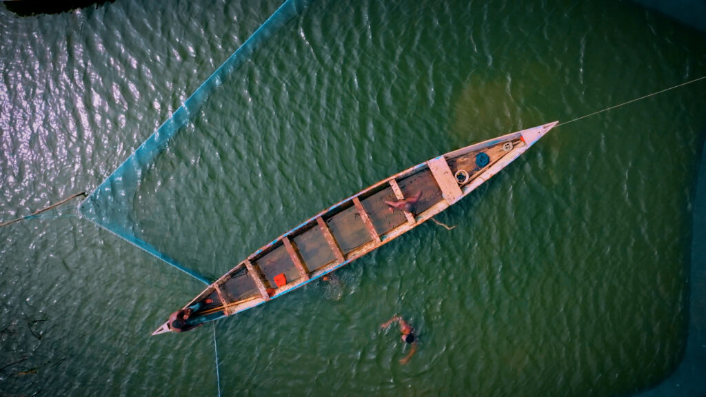 Aerial view of wooden boat with people in green water and fishing net